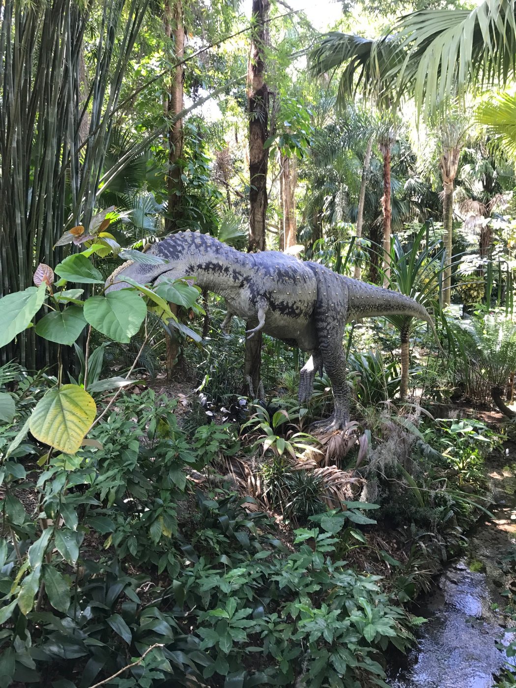 Life-size dinosaur model standing among tropical vegetation